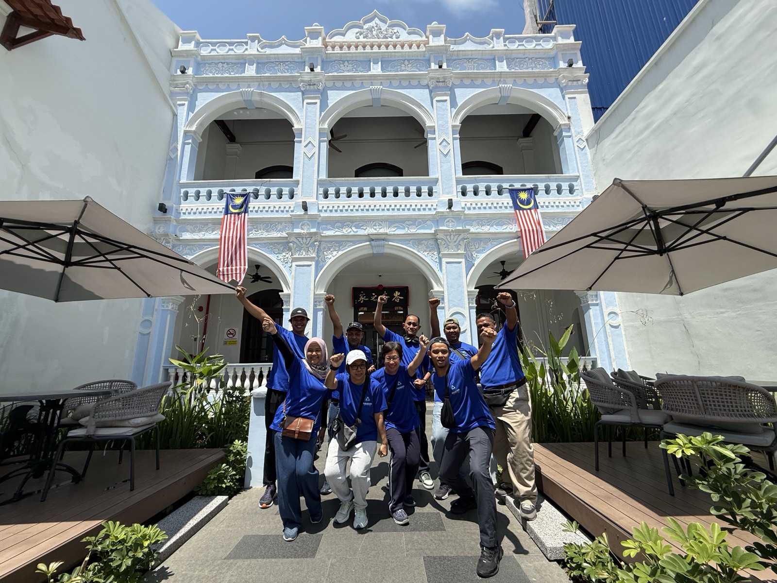 A team cheering with fists raised in front of a heritage mansion