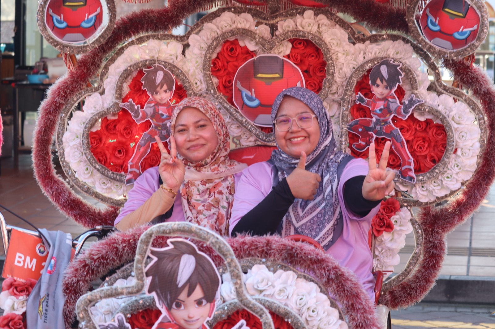 Two participants smiling in a decorated Malacca trishaw