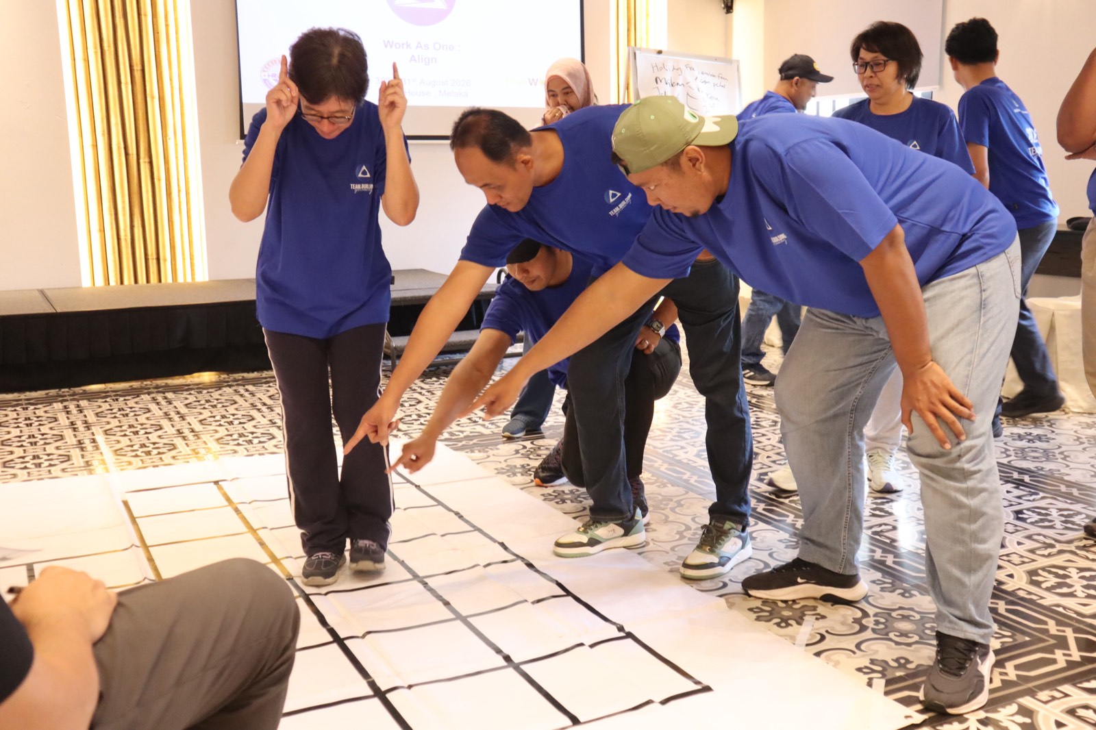 Colleagues in blue t-shirts solving a floor-grid puzzle challenge indoors