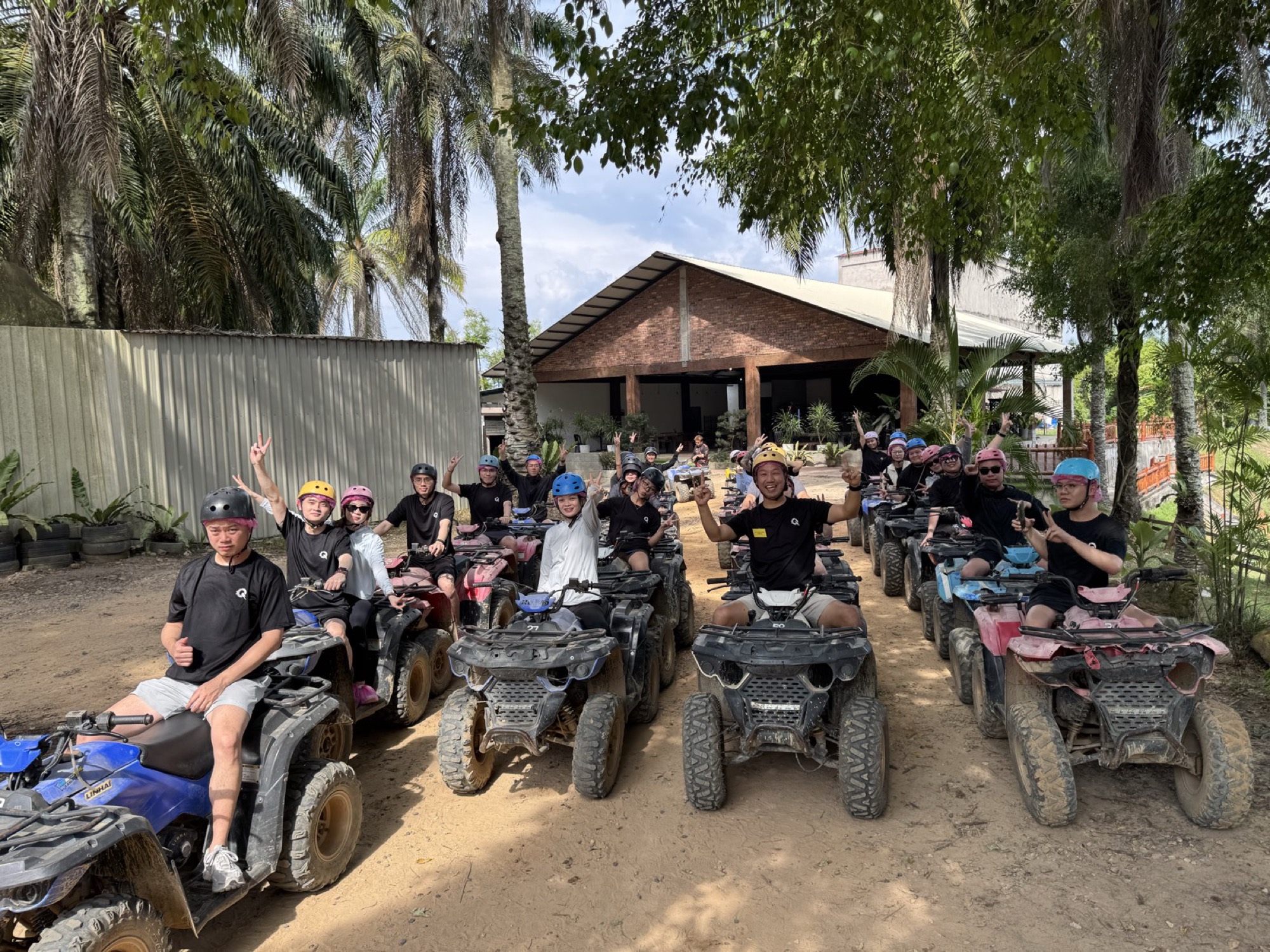 A large group on quad bikes at an outdoor team-building day, arms raised and cheering