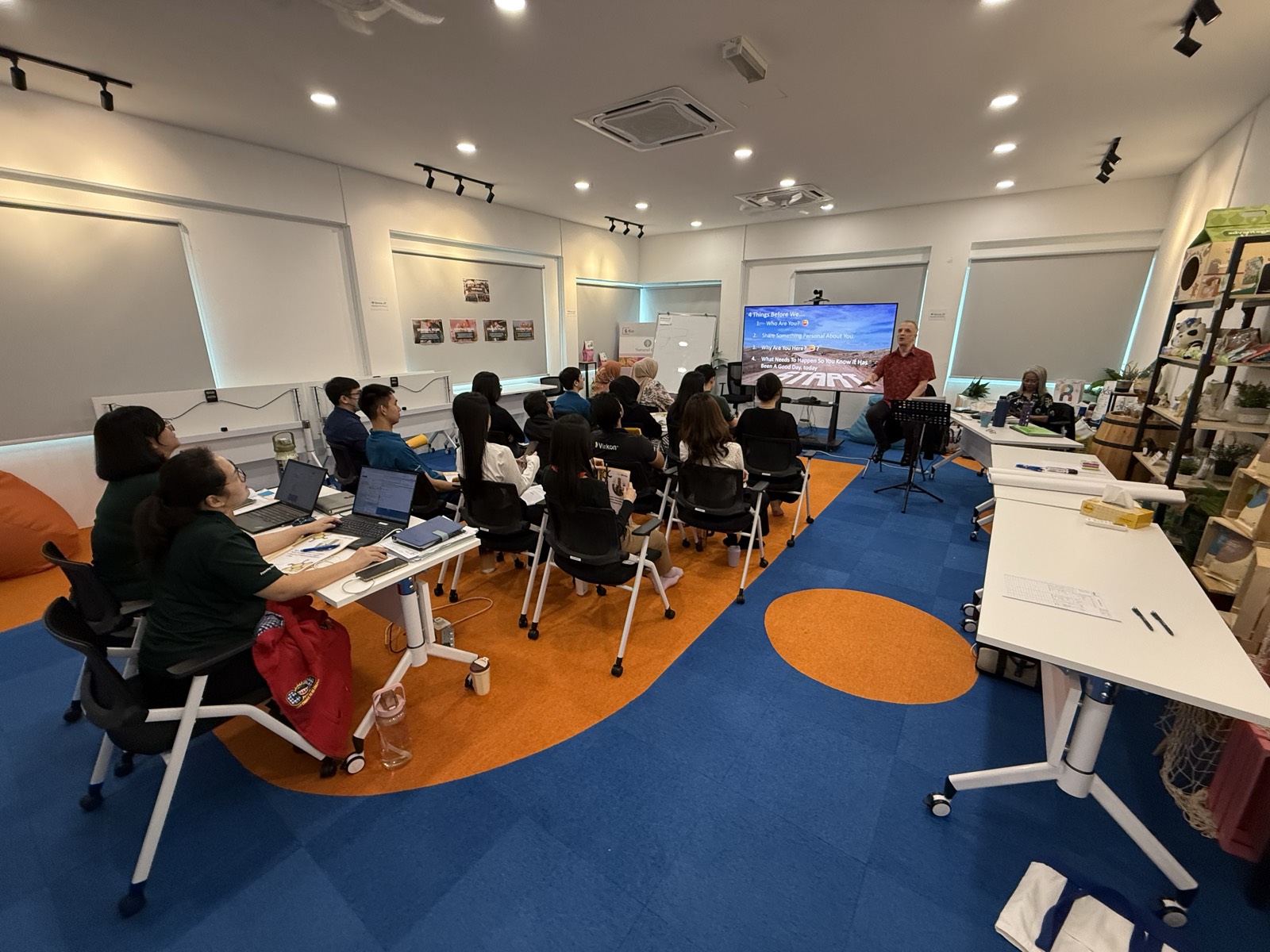 A facilitator leading a soft skills workshop for a seated group in a bright training room