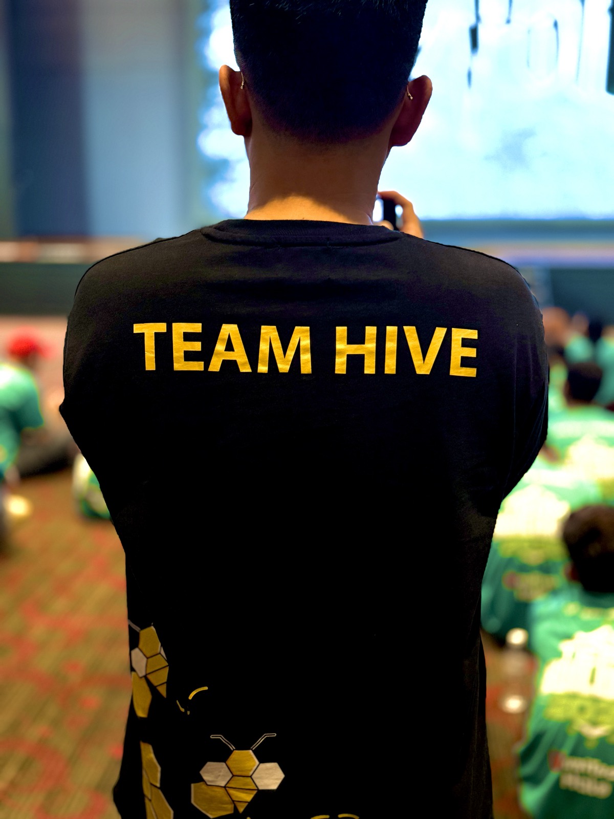 The back of a black &ldquo;TEAM HIVE&rdquo; crew t-shirt with the HiveWorks bee logo, worn at a large company event